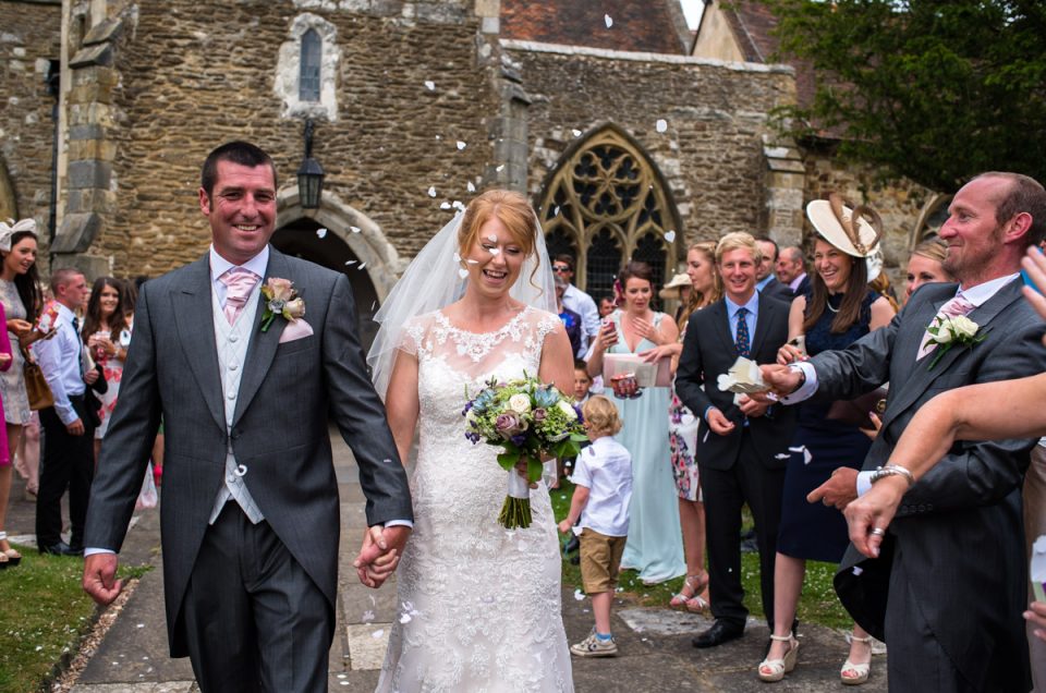 Classic wedding photograph of bride and groom leaving the church under a shower of confetti