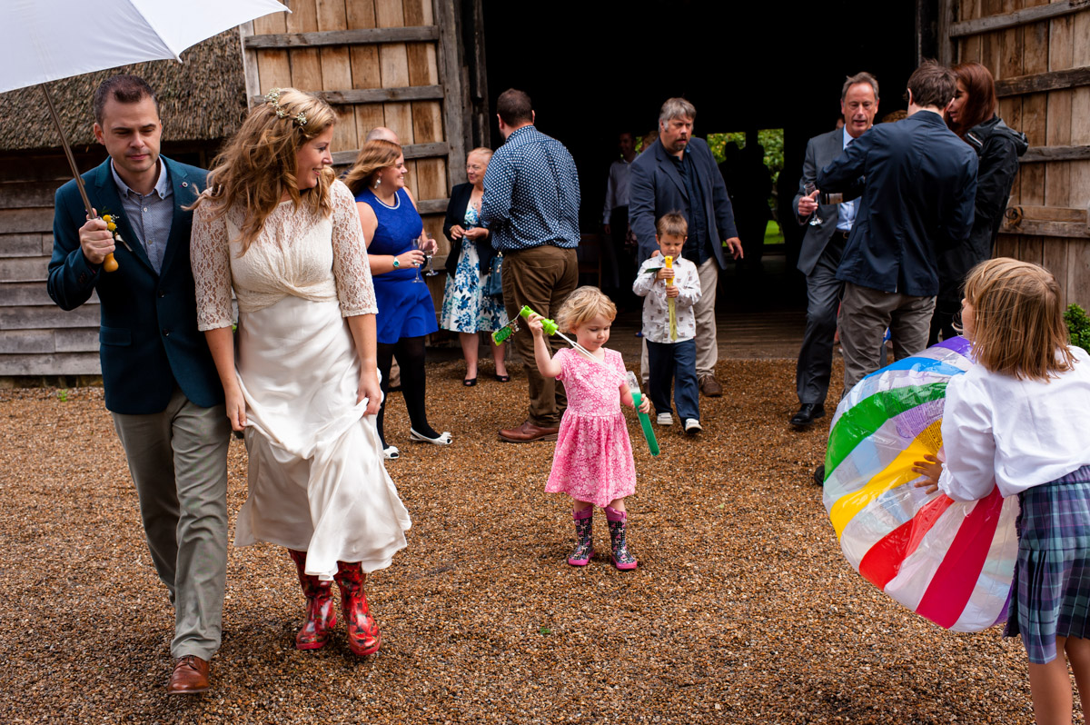 bride and groom outside rats bury barn wedding venue with their guests in the rain