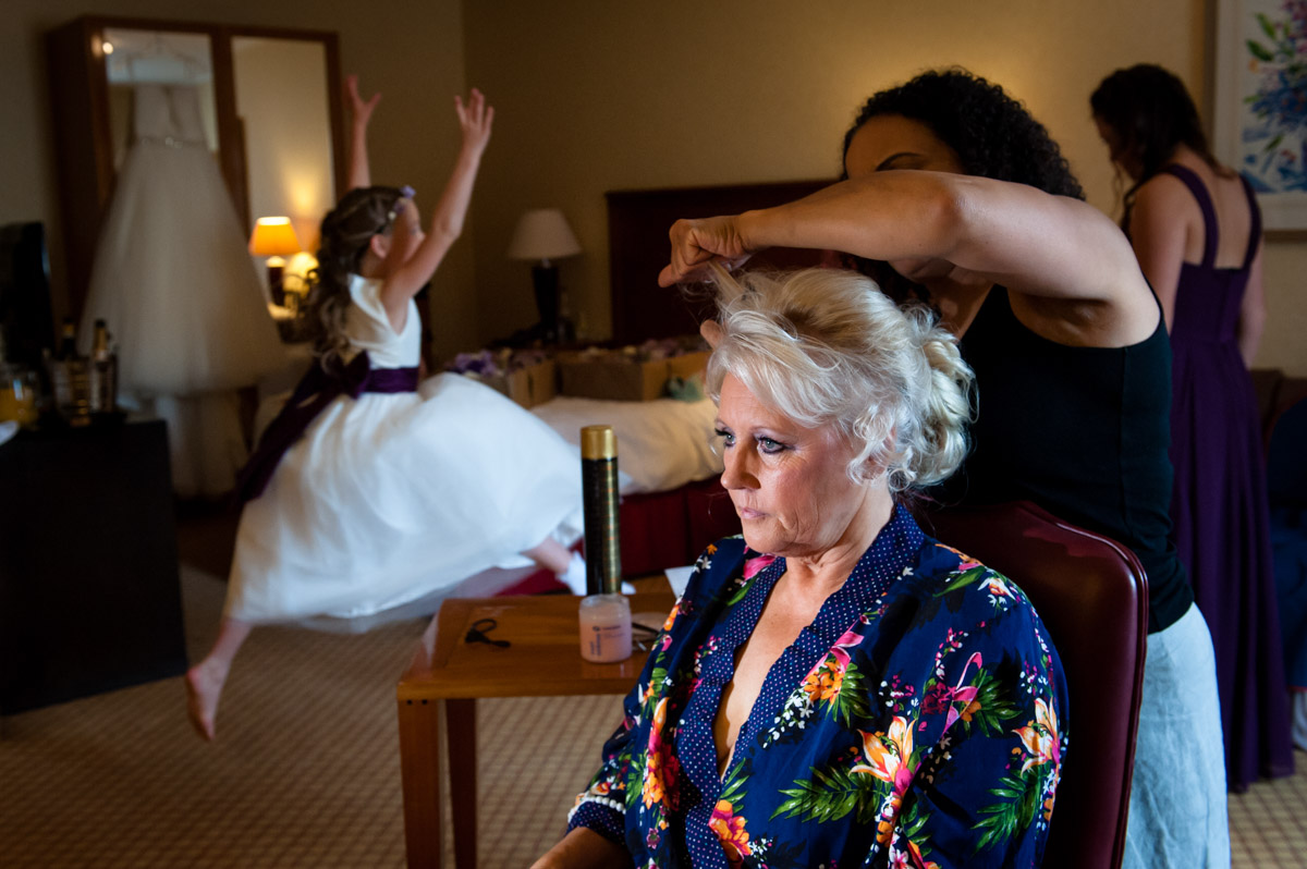little flower girl is photographed jumping while bride has her hair done for her wedding