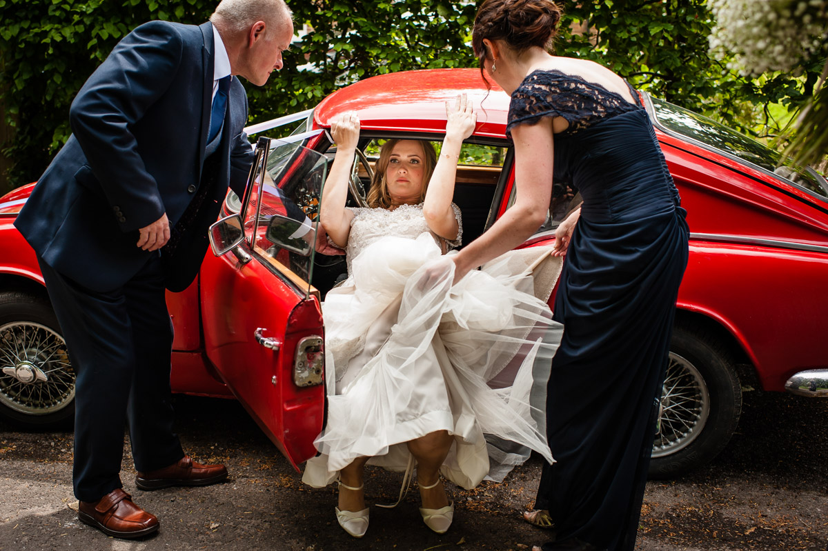 photograph of bride using both hands to get out of her red wedding car