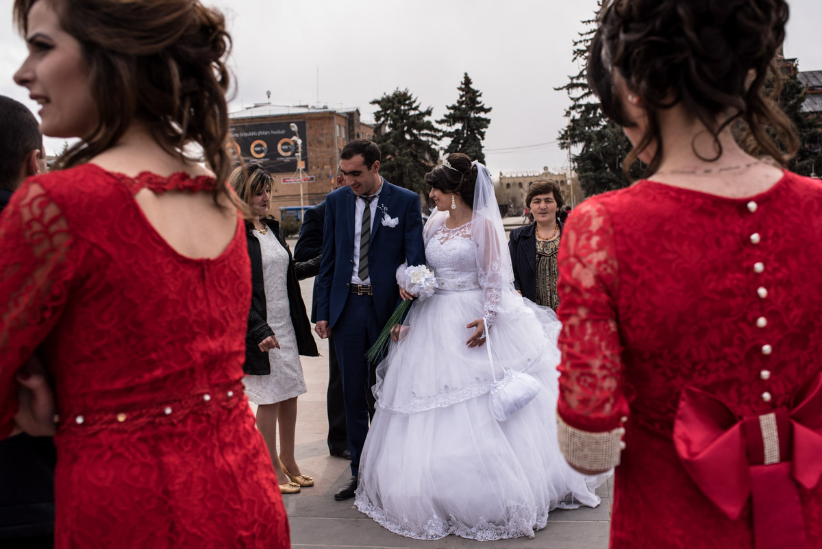 bride and groom and two ladies dressed in red are photographed in gyumri square after their wedding