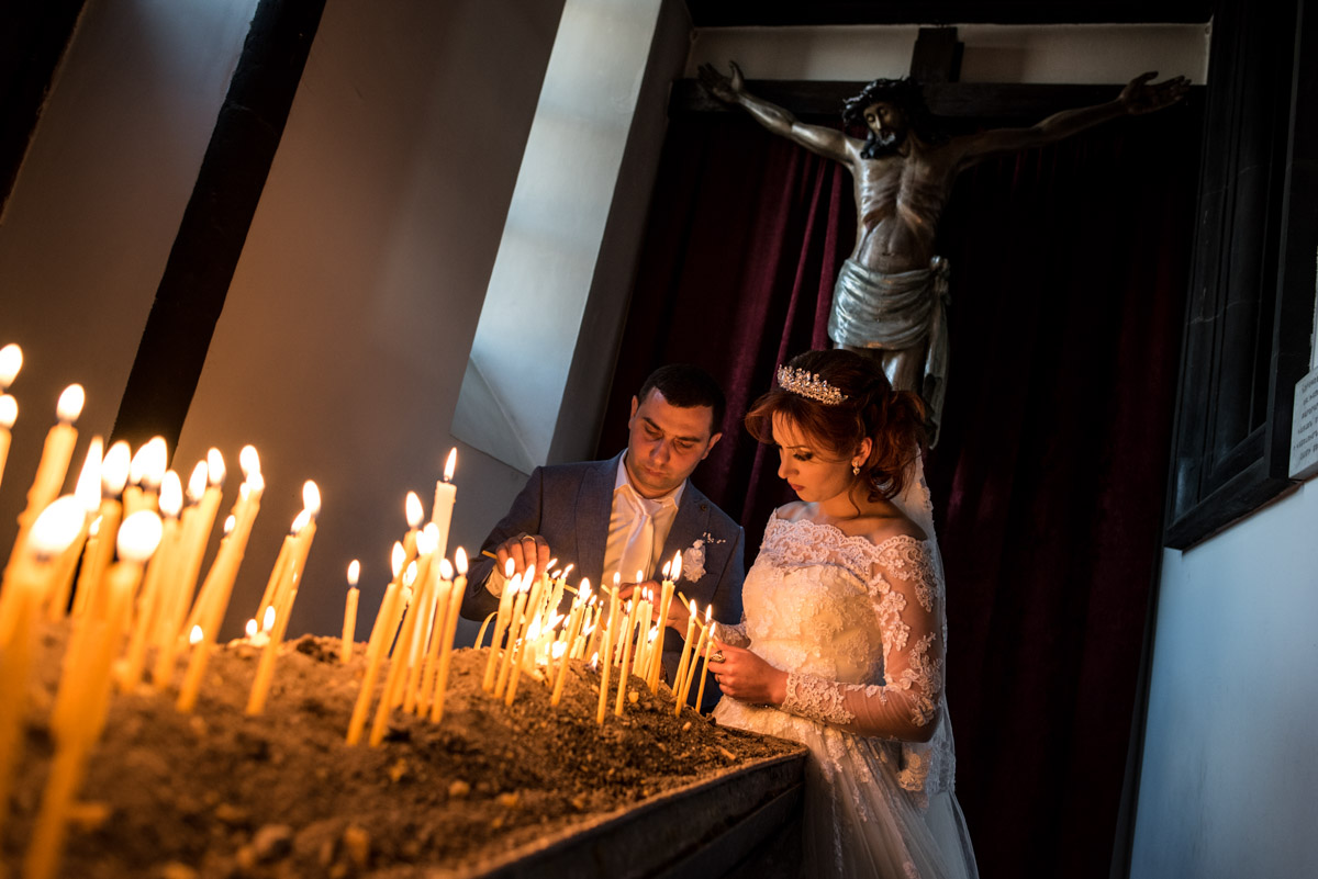 armenian bride and groom light candles on their wedding day with sculpture of christ behind them