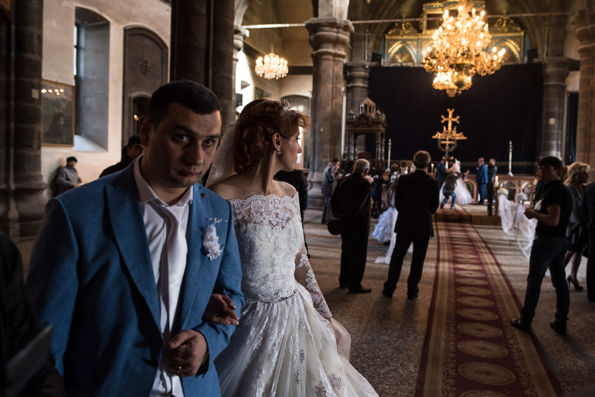 photograph of bride and groom leaving armenian church while another couple are getting married