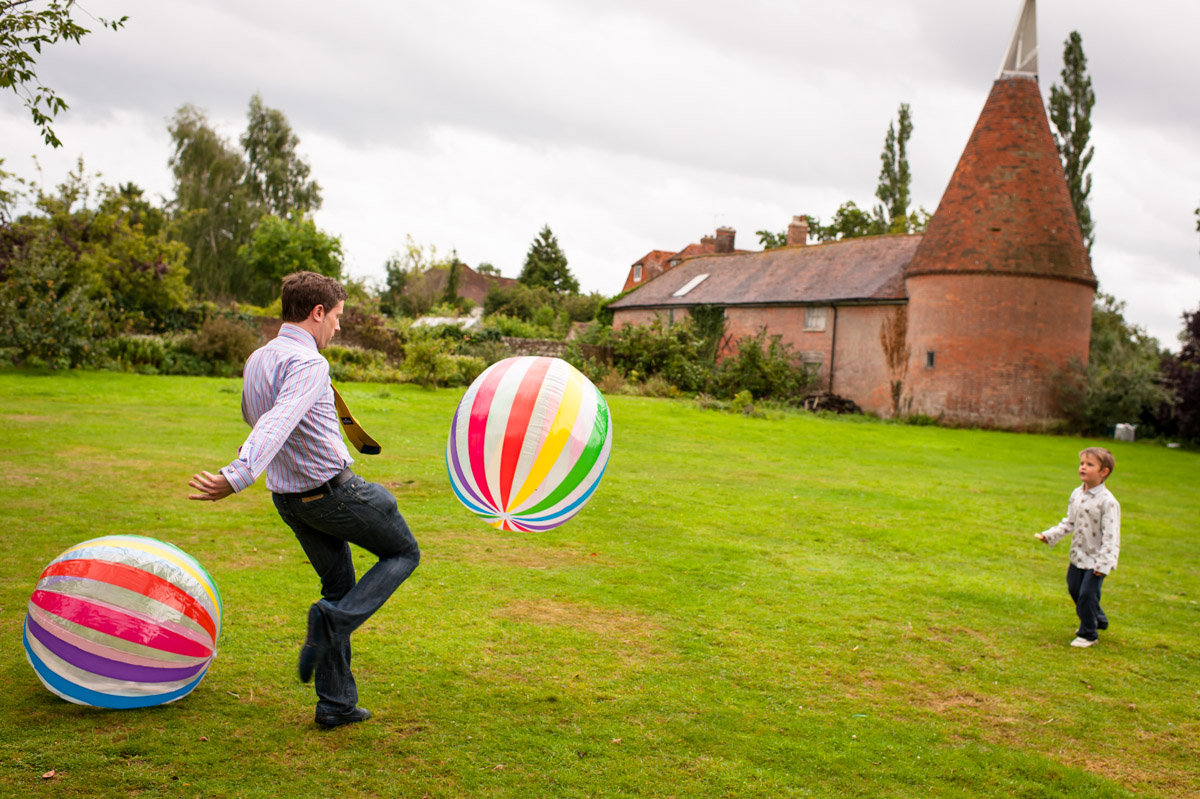 adult and children photographed playing with ball at Ratsbury barn wedding in Kent