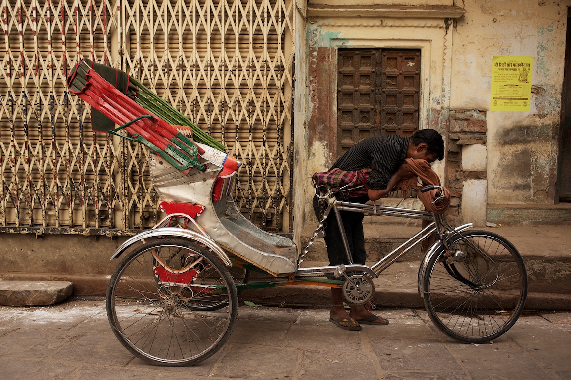 photograph of man wiping sweat from his face by his rickshaw