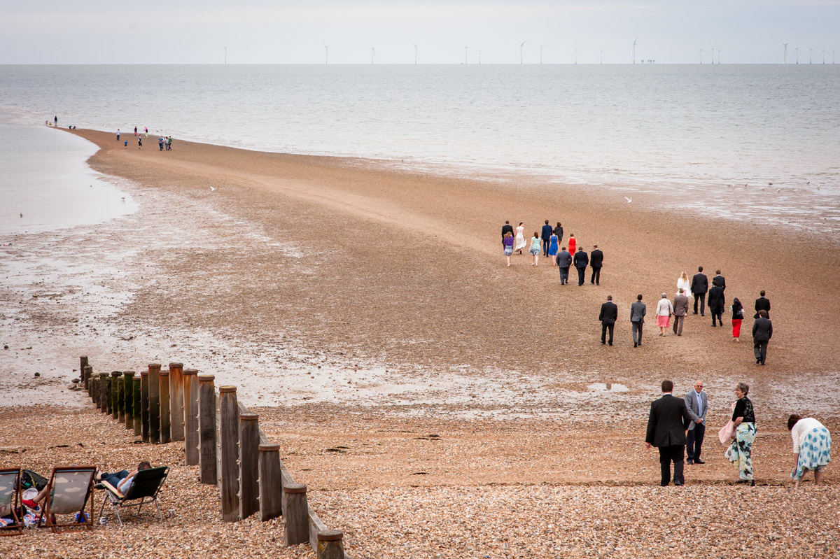Bride and Groom and wedding guests walk down to the beach at Whitstable