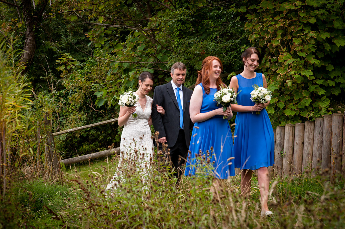 Photograph of Bride, bridesmaids and father walk through garden at The Beacon House