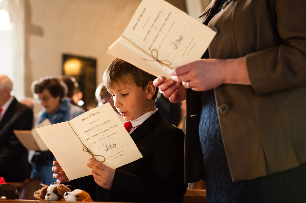 pageboy sings from order of service during charlotte and marks church wedding in kent