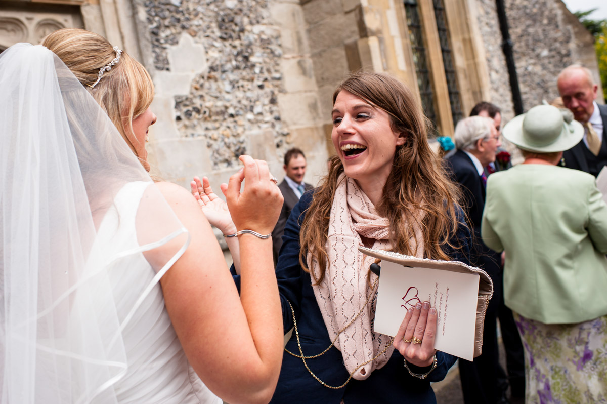 Wedding guest laughs with bride outside church after wedding
