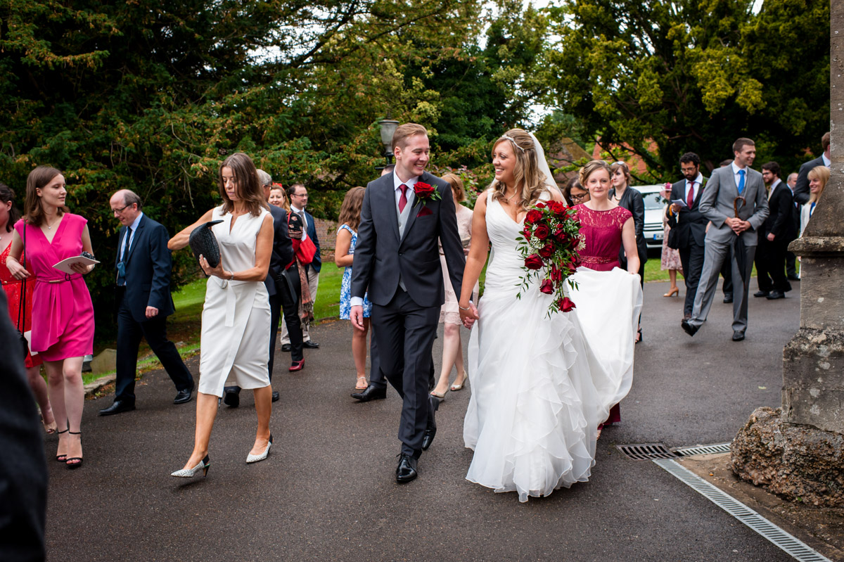 Photo of bride and groom walking down church path with wedding guests