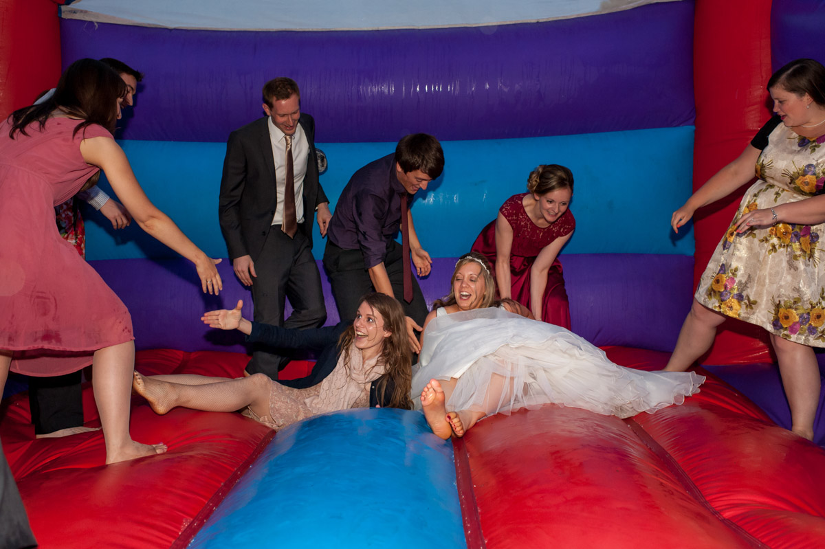 Bride and wedding guest are photographed on bouncy castle at wedding reception