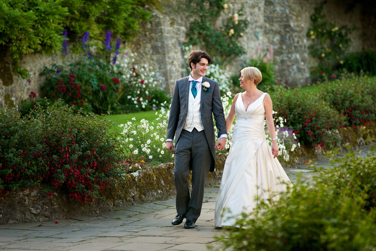 Photograph of Sarah and Leighton walking hand in hand down the pathway at Lympne castle on their wedding day