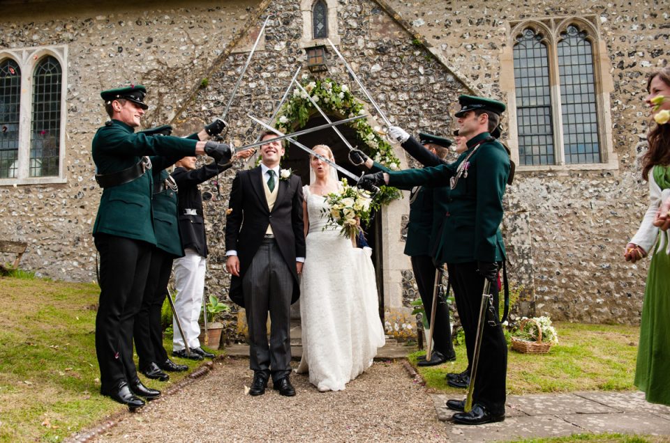 Brdie and groom leave church after their wedding under swords held by army friends