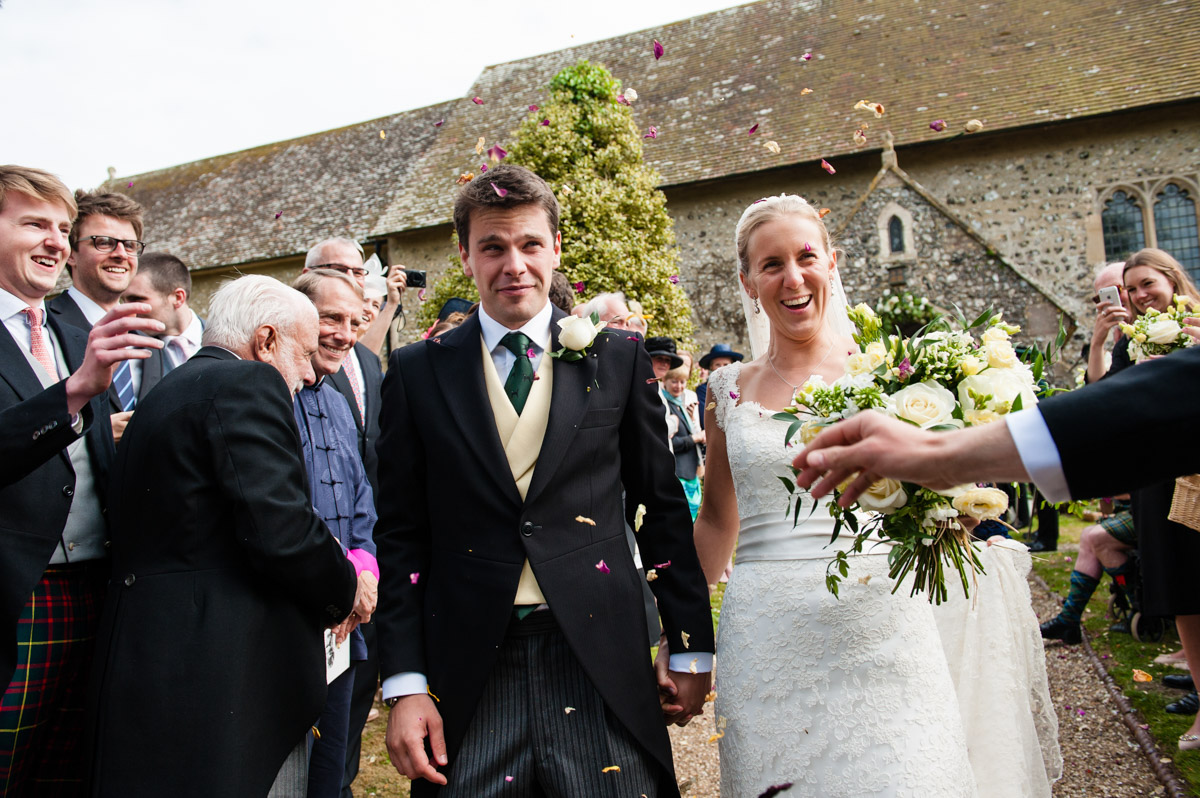olivia and nick have confetti thrown over them while leaving petham church after their wedding ceremony