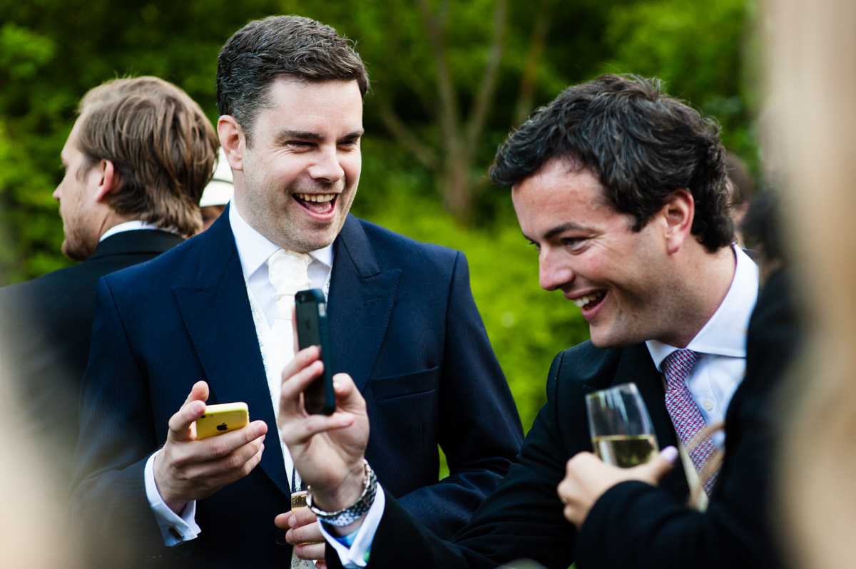 wedding guests are photographed laughing at their phone pictures
