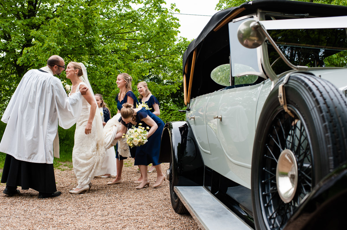Olivia the bride arrives for her wedding in vintage car, bridesmaids hold up her tain