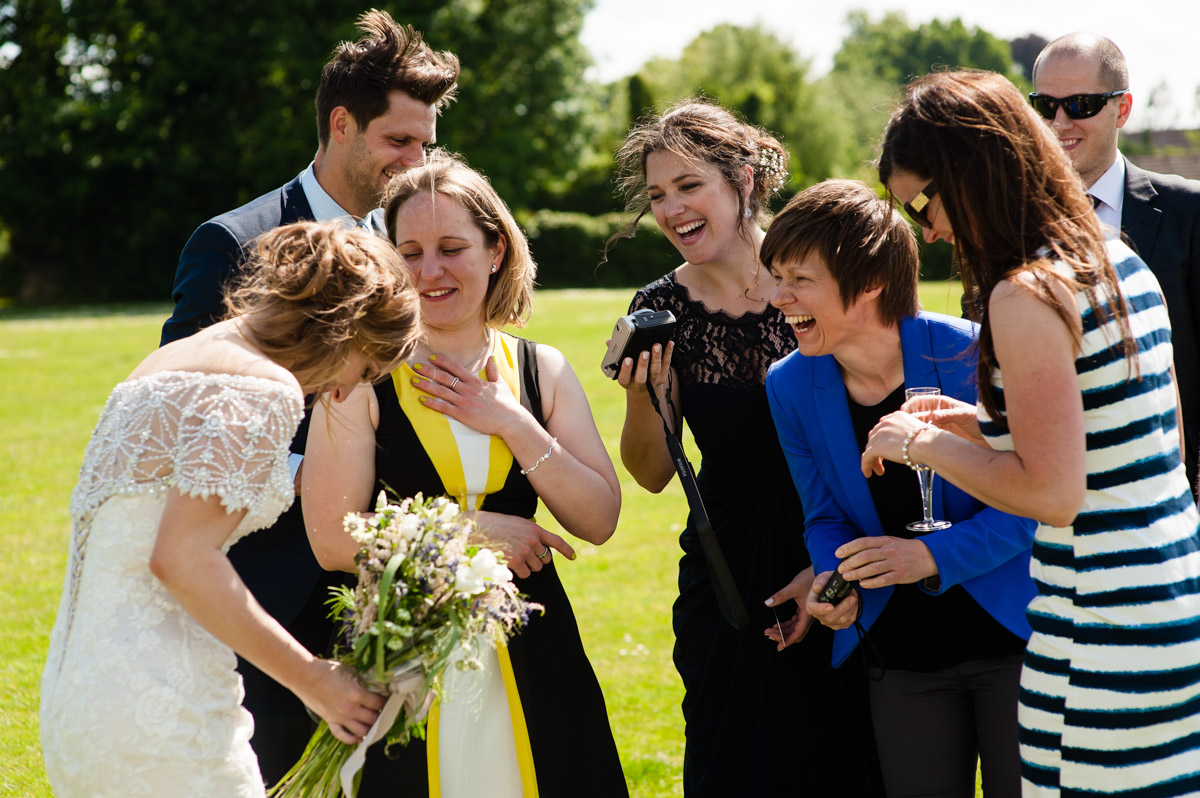 friends of catherine laugh with her at her wedding reception on village green in kent