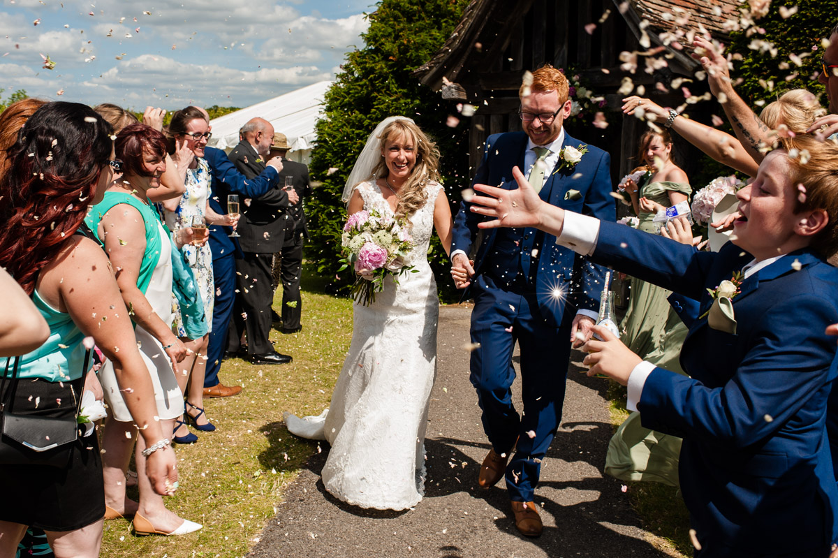Guests throw confetti over mark and selina after their wedding ceremony at st augustines priory in kent