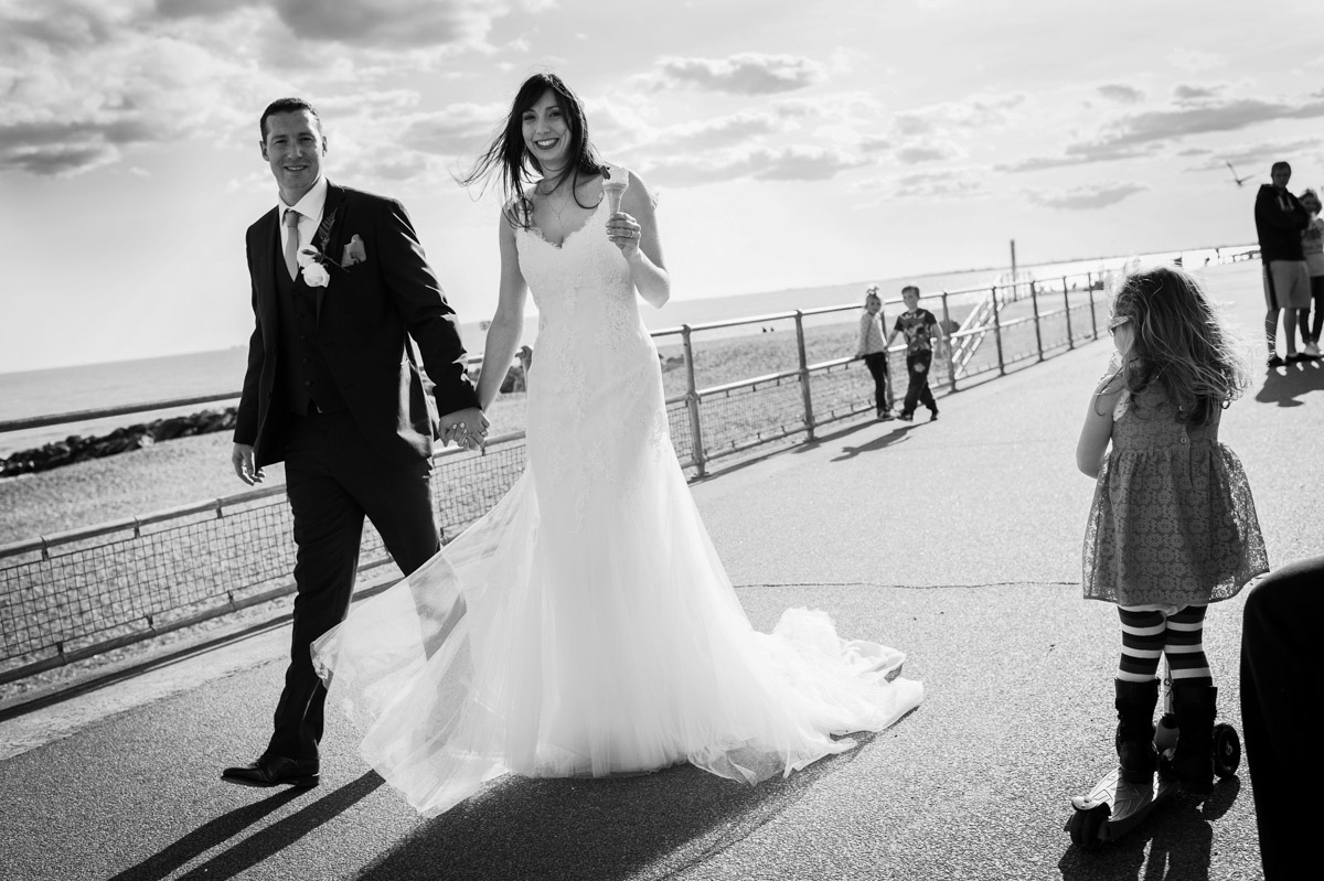 Bride and groom walk hand in hand along Hythe seafront after getting an ice cream