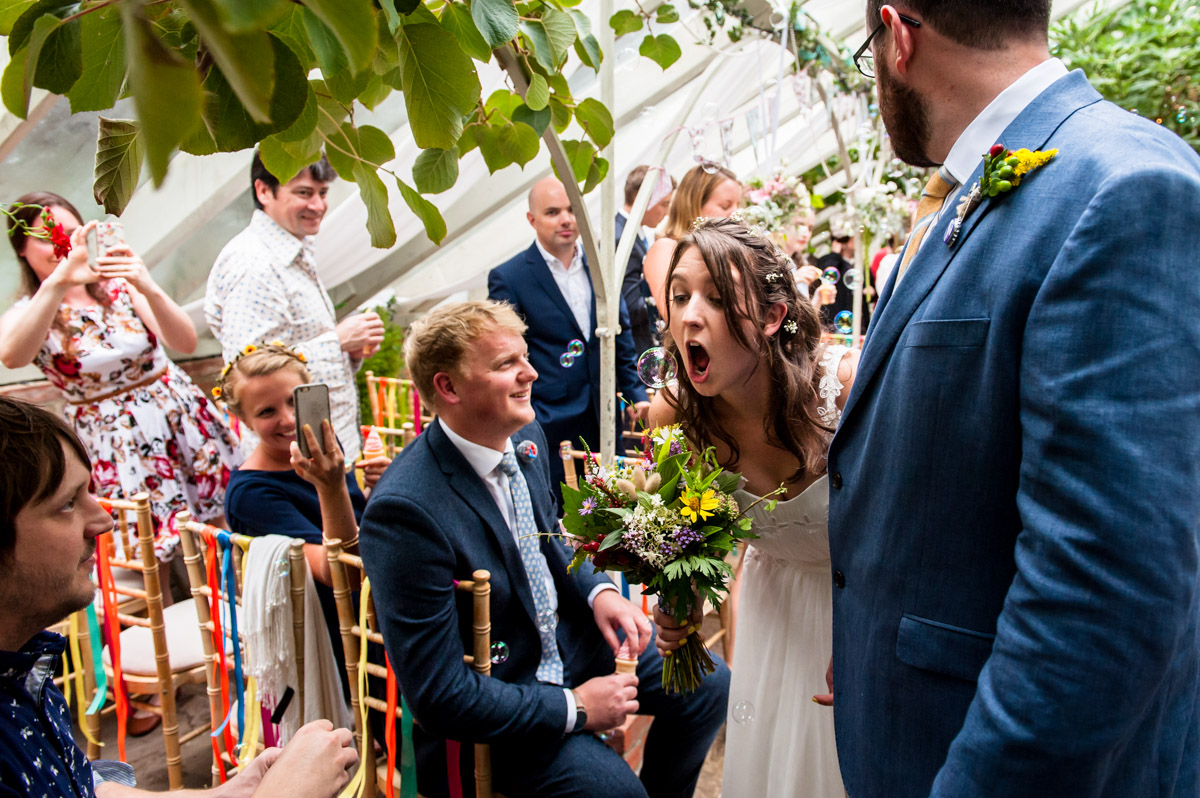 bride pretends to catch bubbles at wedding in the glass house at the secret garden kent