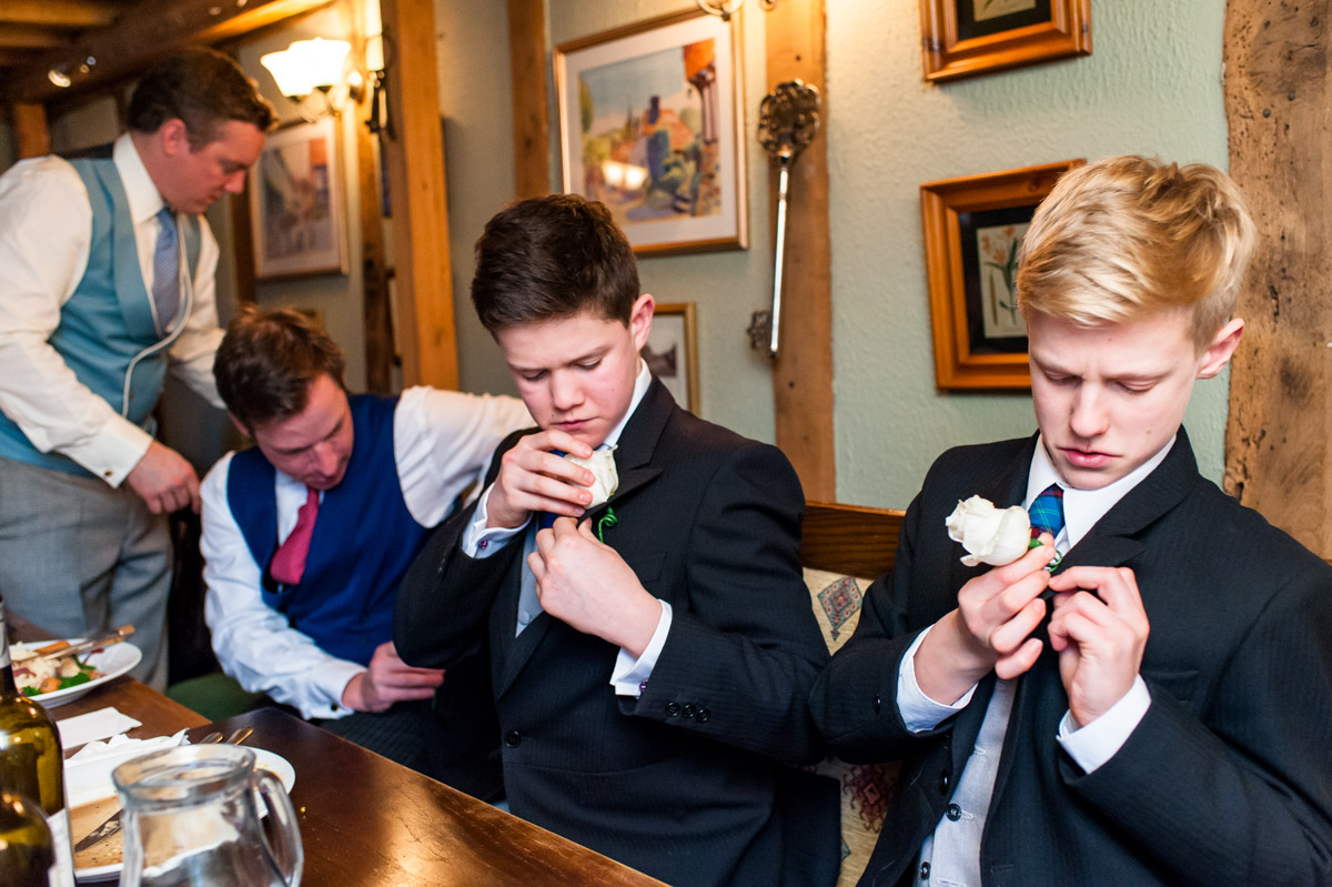 Young groomsmen fit their button holes at the pub before Marcus and Frances's church wedding in Elham