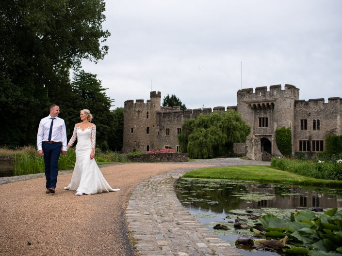 Lexy and Paul walk hand in hand by Allington Castle near Maidstone in Kent after their wedding ceremony