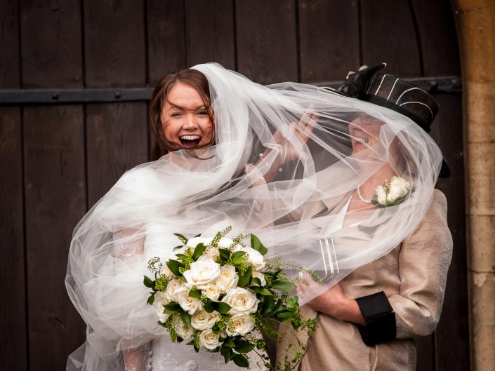 Emmas veil catches in the wind and is photographed blowing into her mums face after Kent church wedding near Maidstone