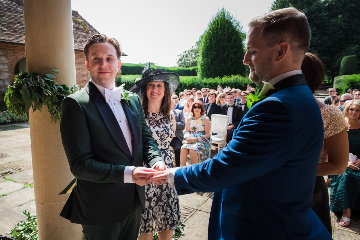 wedding photograph of David putting the ring on Simons finger during their ceremony at Port Lympne in kent