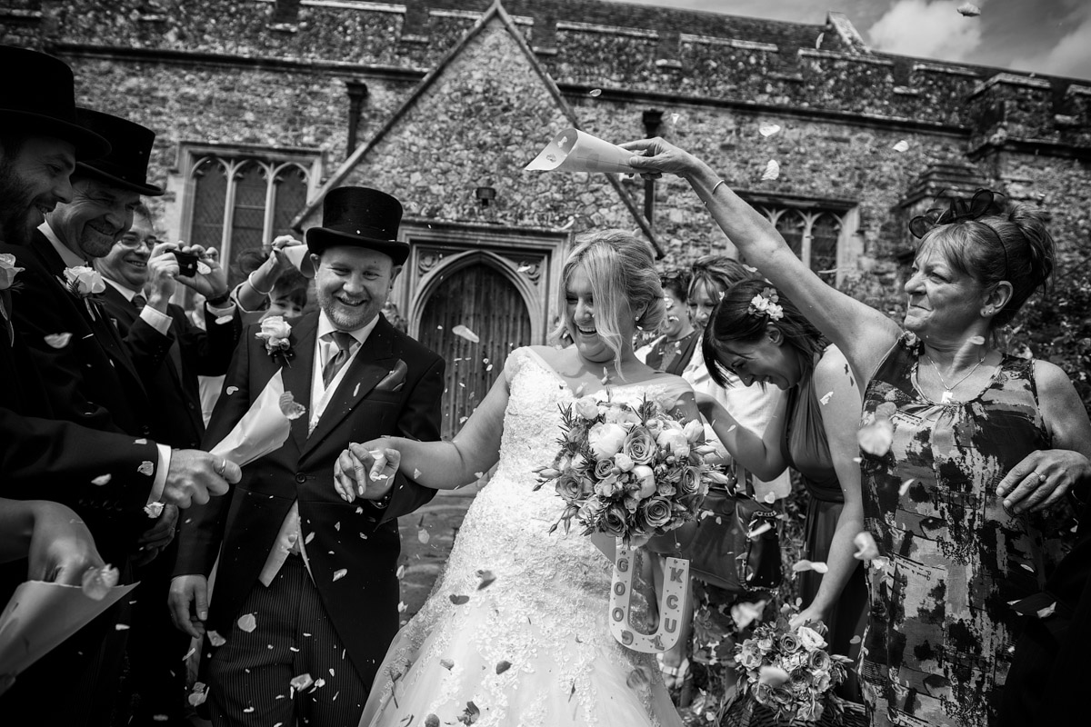 Blacka nd white wedding photograph of Kate and Ryan being covered in confetti at the church