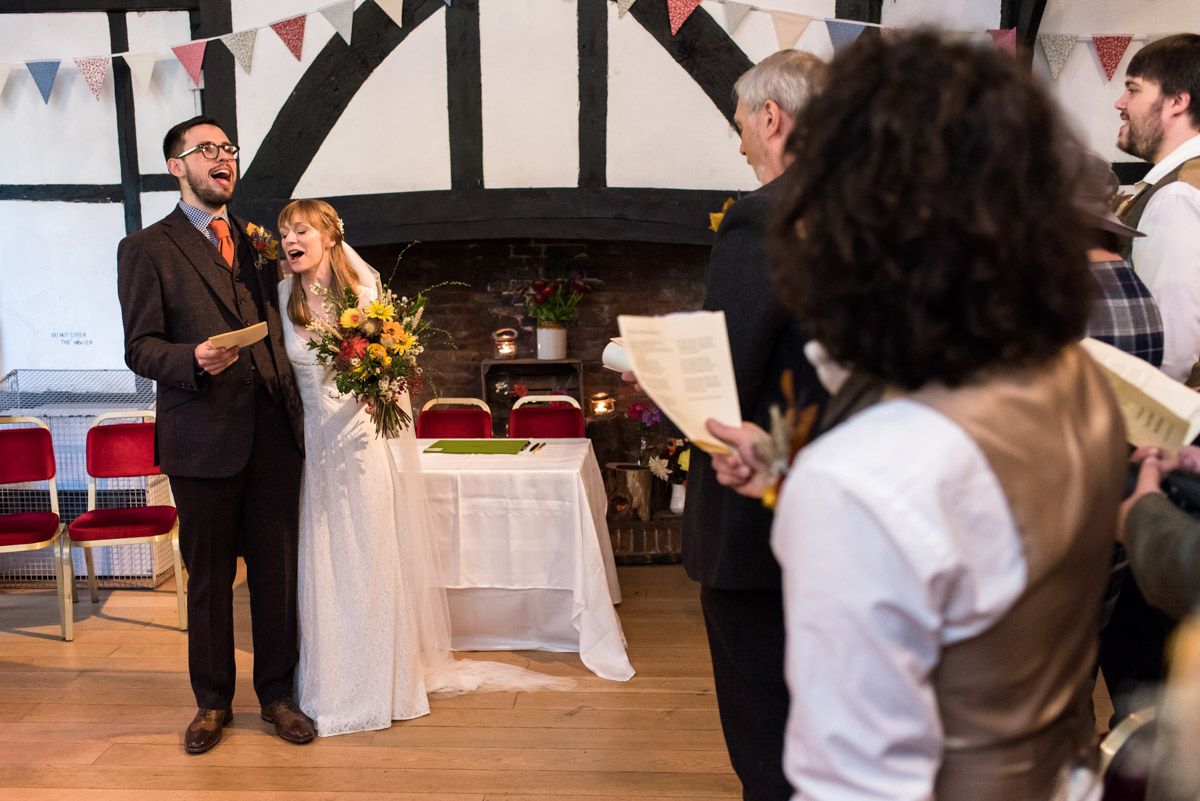 Paul and Laura and their wedding guests are photographed singing after the ceremony. Kent wedding photography at Chilham Village Hall