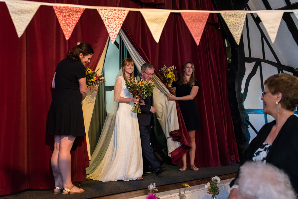 Laura and her bridesmaids are photographed on the stage before the wedding ceremony at Chilham Village hall in Kent