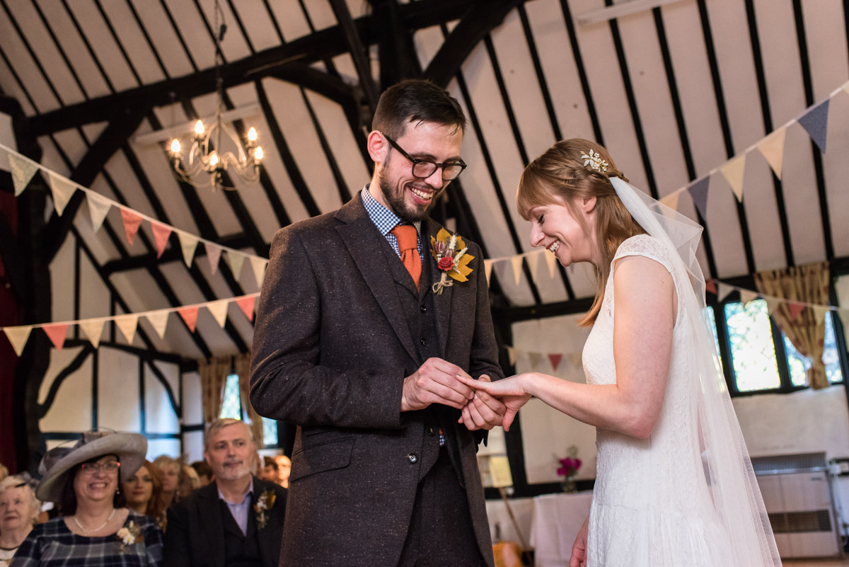 Kent wedding photography at Chilham Village Hall, Paul placing the wedding ring on Lauras finger during ceremony