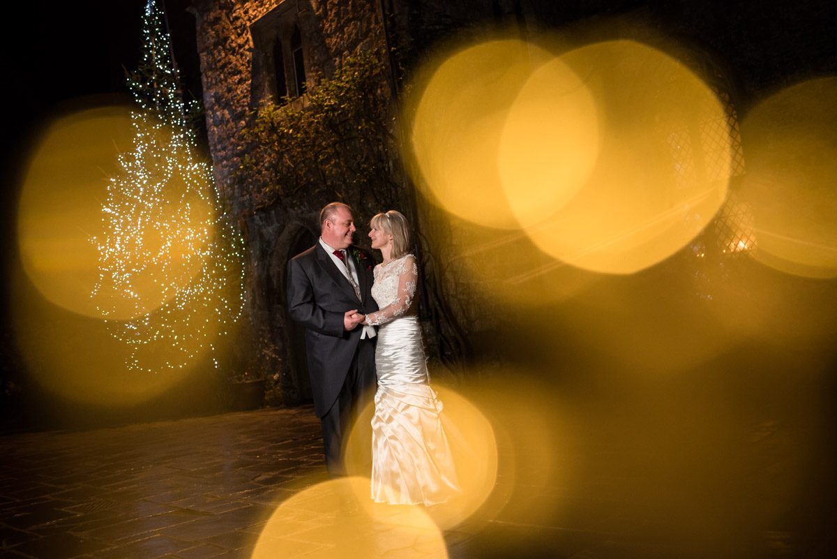 Portrait of sue and Nick outside Lympne Castle with christmas lights on their wedding day