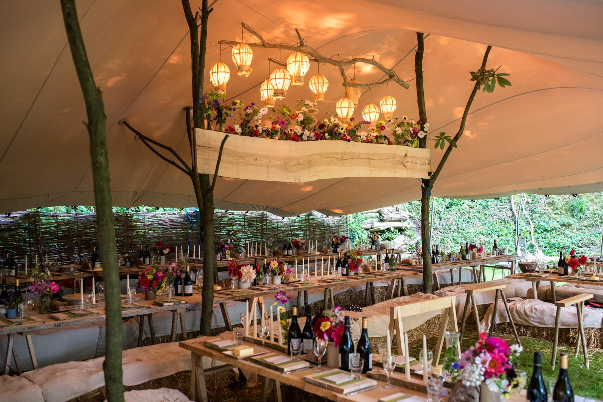 Wedding details and decorations adorn the wooden tables and stretch tarpaulin roof at Seb and Brogans party venue