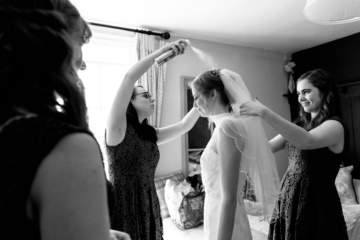 Bridesmaids are photographed applying hairspray before Beth and Toms Ratsbury Barn wedding in Kent