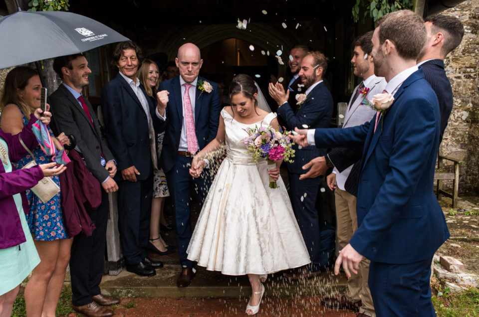 Photograph of Emily and Tom leaving the church under confetti after their wedding ceremony