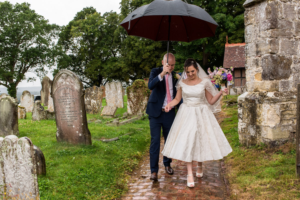 Photograph of Tom and Emily under umbrella after their church wedding