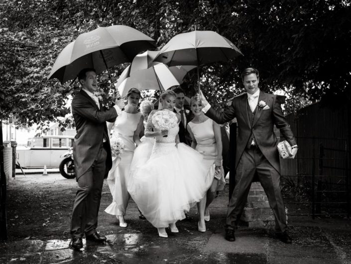 Photograph of Rebecca arriving for her Smarten church wedding in Kent being sheltered from the rain