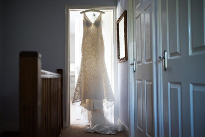 Lace long wedding dress photographed hanging from door frame