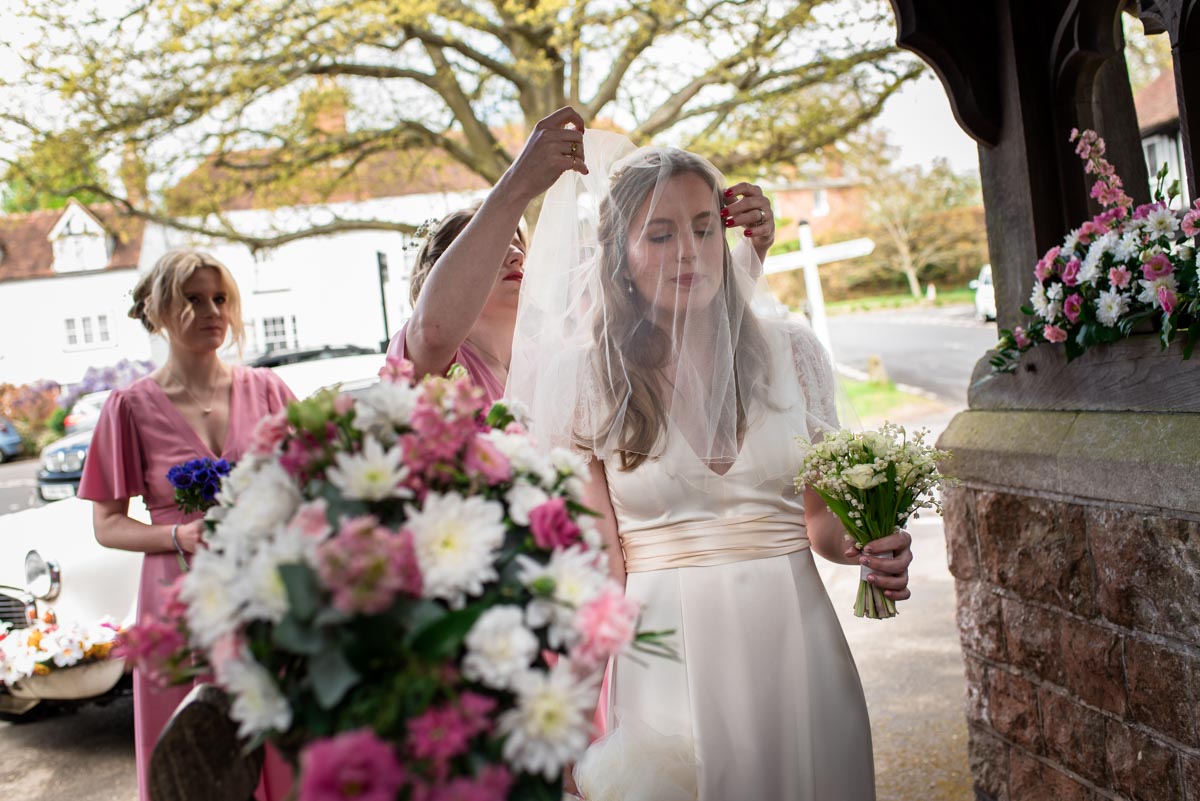 Bridesmaid places veil over brides face before her walk into the church