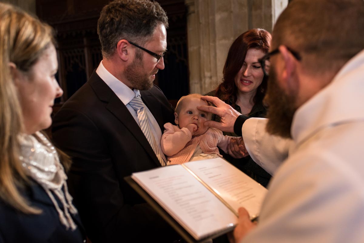Kent christening photography. The vicar blessing Emily