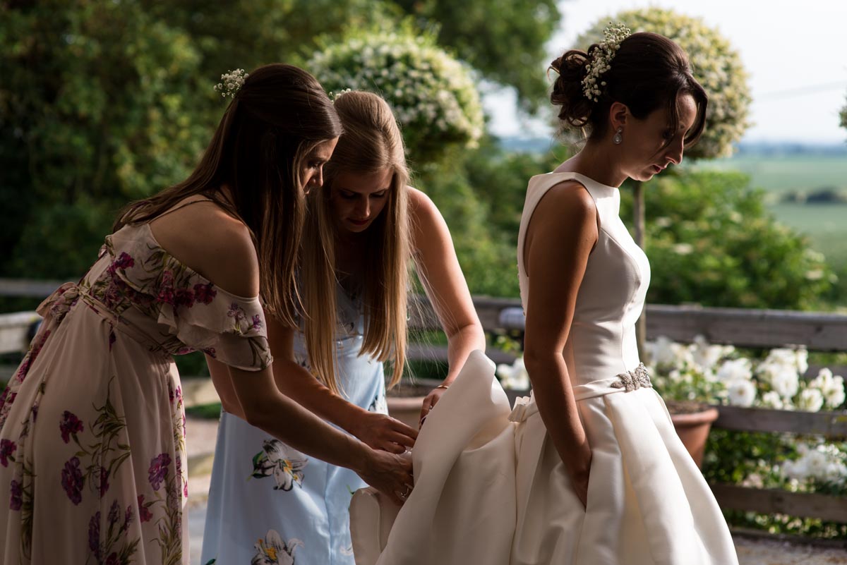 Bridesmaids adjust Sarah's wedding dress at Odo's Barn in Kent