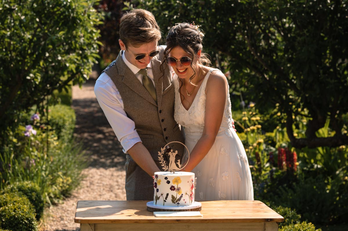 fred and becca photographed cutting their wedding cake at the secret garden in kent