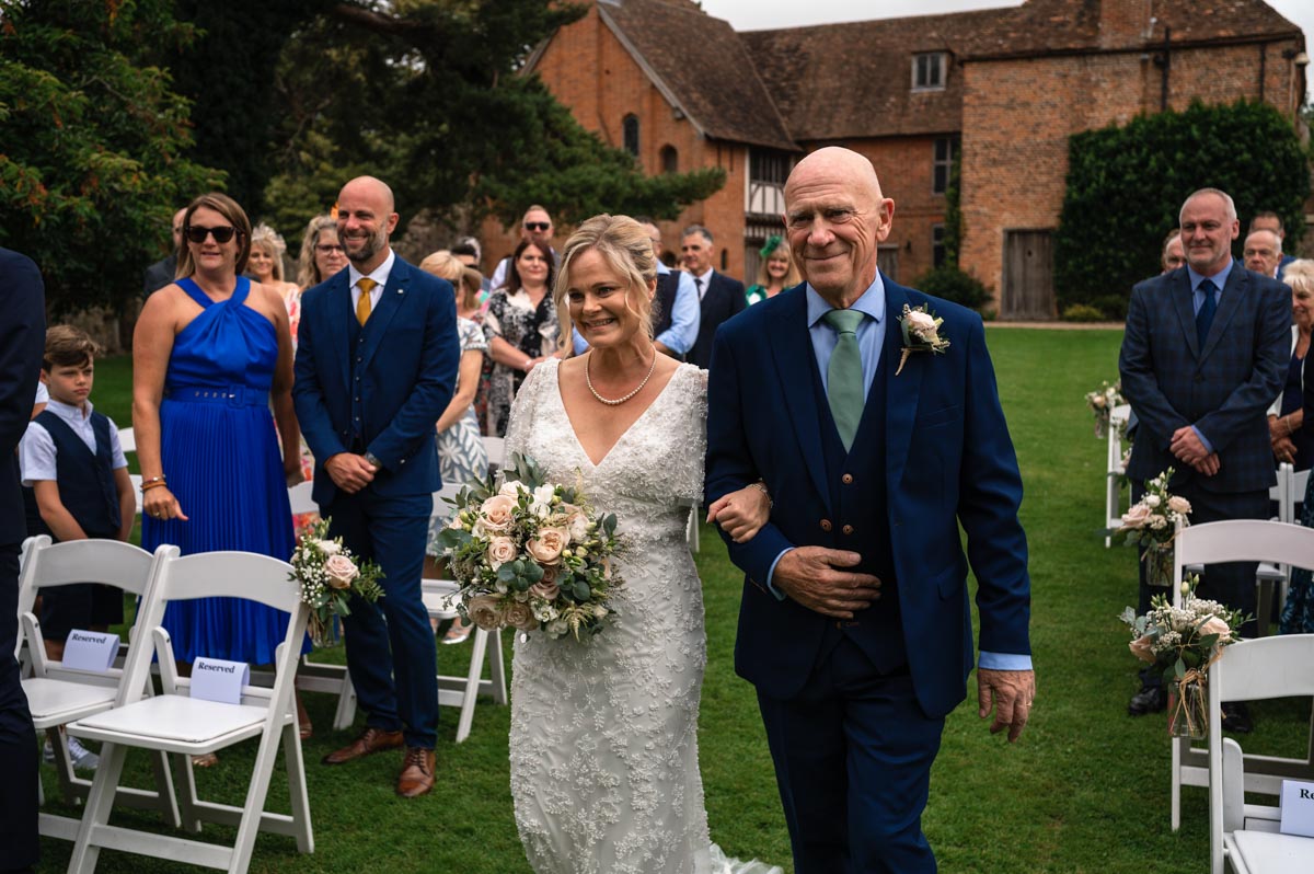 Lara and father walk down the aisle during outside ceremony at westenhanger castle wedding venue in kent