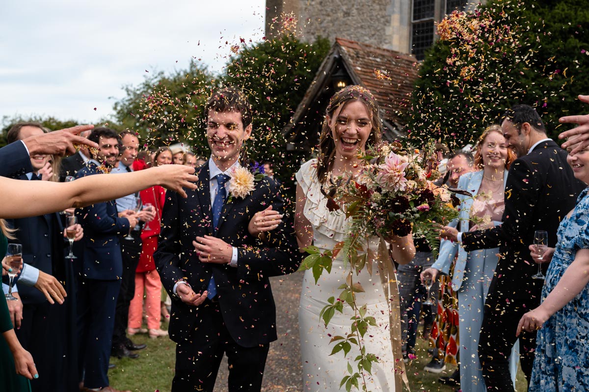 Poppy and Pablo walk through confetti after their kent wedding ceremony at Bilsington Priory